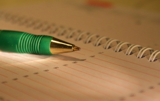 close up of a green pen resting on a spiral notebook