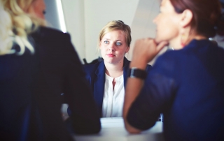 young female in business attire sitting across the table from two business professionals