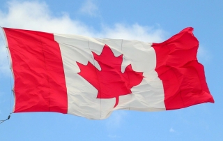 a Canadian flag blowing in the wind against a blue sky
