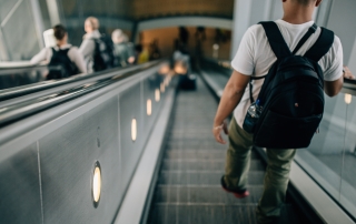 young man wearing a black backpack walking down an escalator