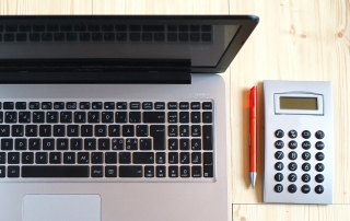 an open laptop computer with a calculator and red pen beside it