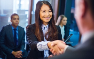 young woman in business attire, holding a portfolio shaking hands with another professional