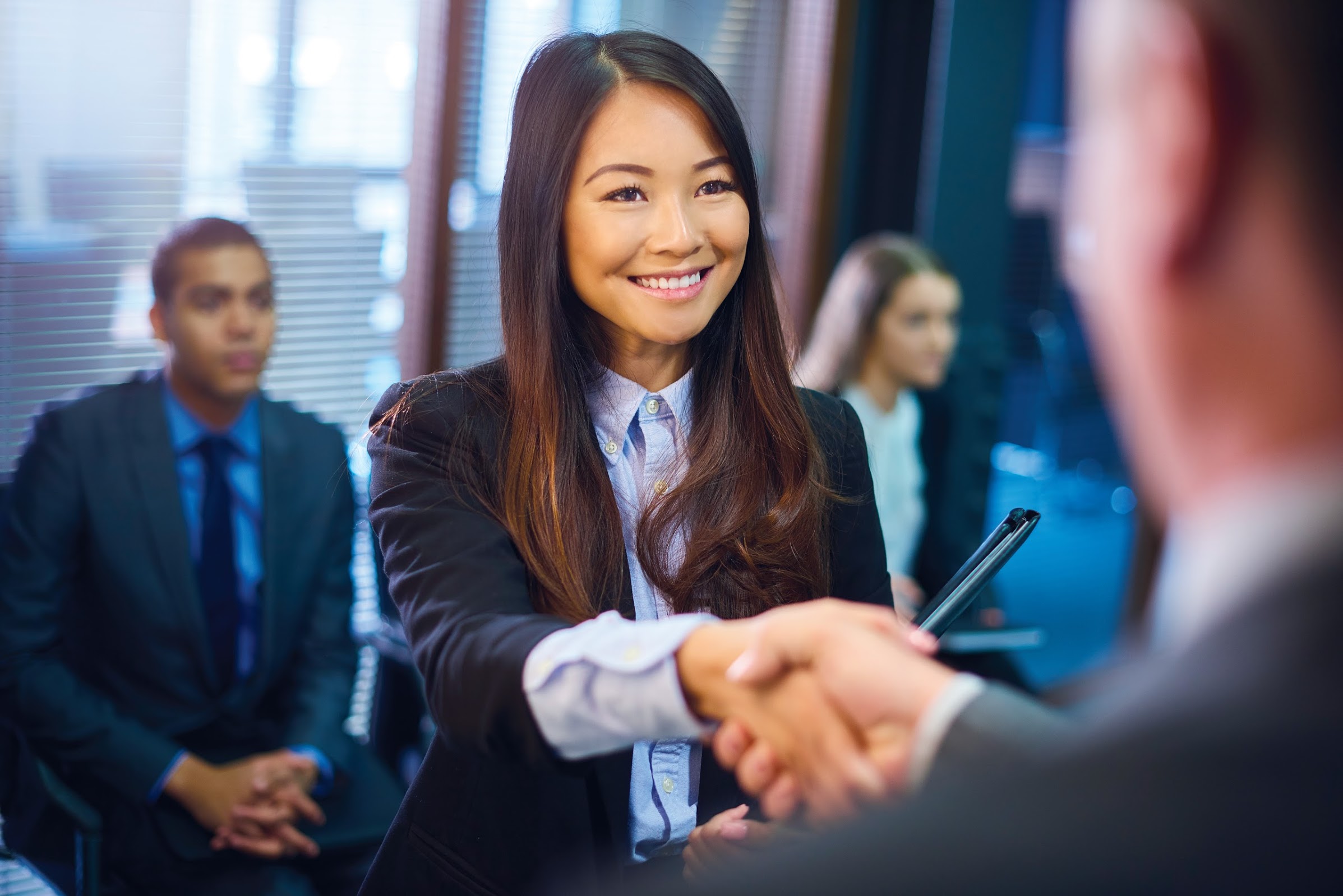 young woman in business attire, holding a portfolio shaking hands with another professional