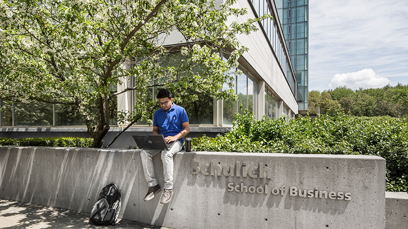 Male student using a laptop while sitting outside of Schulich School of Business